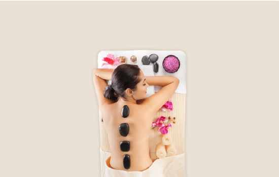 Banner com mulher deitada confortavelmente em uma sessão de massoterapia com pedras quentes, fundo bege claro